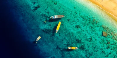 Vista aérea de barcos en aguas costeras turquesas junto a una playa de arena