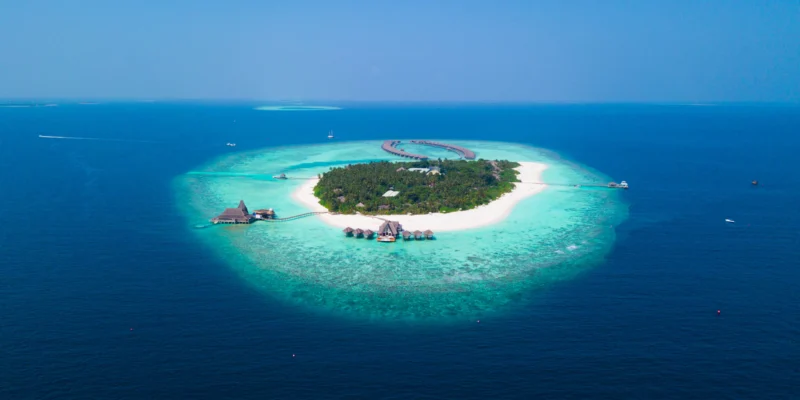 Vista aérea de una isla arbolada con playa blanca y laguna turquesa en Maldivas
