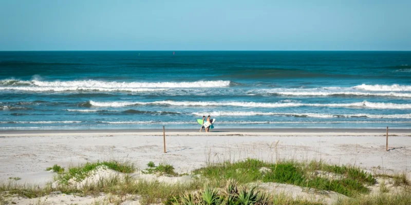 Dos personas con tablas de surf en New Smyrna Beach, con olas rompiendo al fondo