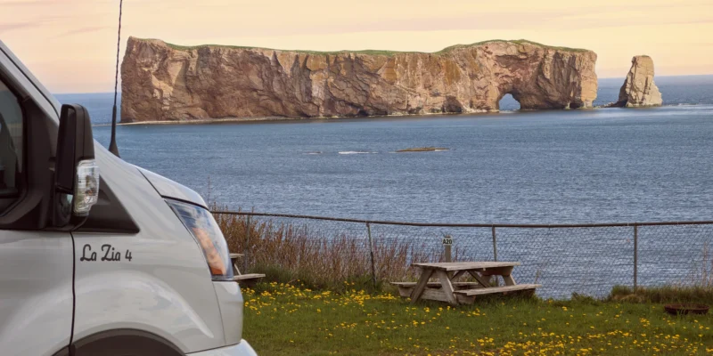 Furgoneta cámper y mesa de pícnic en la costa con vistas a la roca Percé en Québec