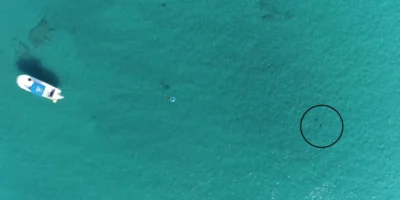 Vista aérea con dron del montaje experimental frente a Florida, con un barco, un altavoz submarino y un tiburón señalado con un círculo negro.