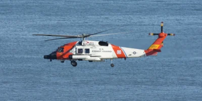 Helicóptero blanco y naranja de la Guardia Costera de Estados Unidos volando sobre el mar azul. Imagen ilustrativa de archivo de 2021; no muestra el rescate frente a Ensenada de octubre de 2026.